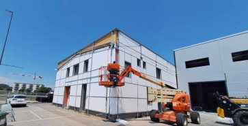 Aerial work platform beside an industrial building during facade installation works.